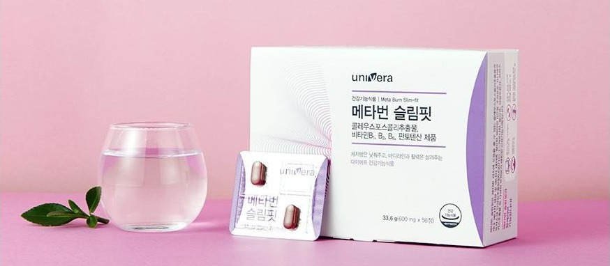 핑크 벽 앞 핑크 바닥 위에 놓인 메타번 슬림핏 패키지와 그 앞에 기대 세운 PTP 1장, 왼쪽에 물이 담긴 둥근 유리컵과 초록 잎가지. 패키지 글자: univera, 건강기능식품 | Meta Burn Slim-fit, 메타번 슬림핏, 콜레우스포스콜리추출물, 비타민B1, B2, B6, 판토텐산 제품, 체지방은 낮춰주고, 바디라인과 활력은 살려주는 다이어트 건강기능식품, 건강기능식품 마크