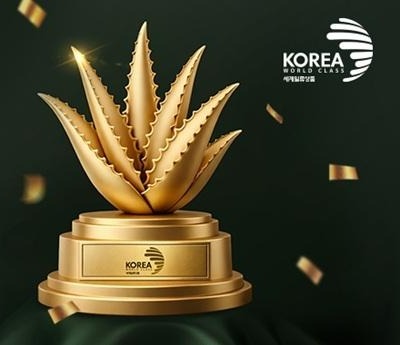 받침에 KOREA 세계일류상품 표시가 새겨진 금색 알로에 트로피와 흩날리는 금박, 오른쪽 위에 KOREA WORLD CLASS 세계일류상품 마크
