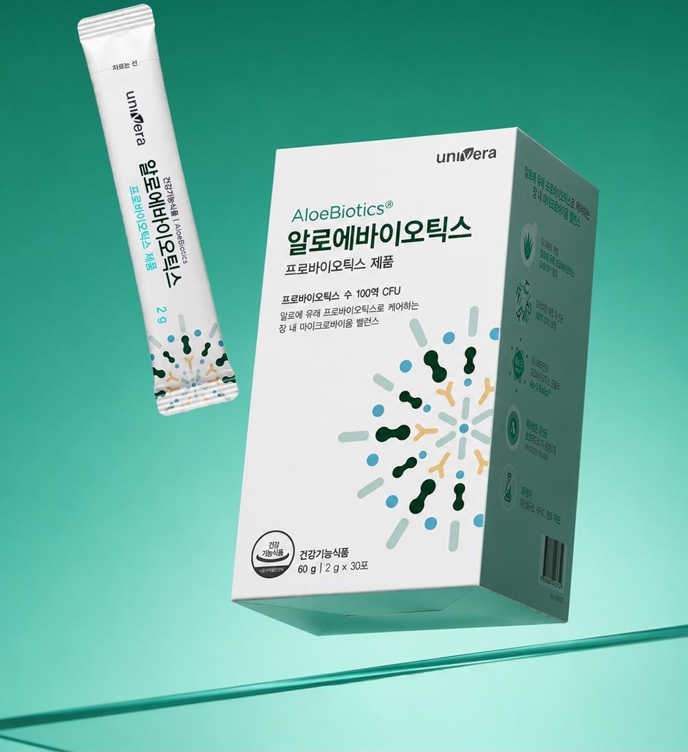 초록 그라데이션 지면 위에 비스듬히 떠 있는 알로에바이오틱스 스틱과 상자, 아래에 유리판