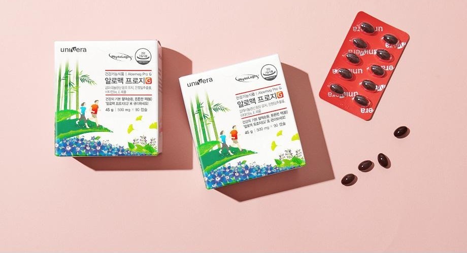 알로맥 프로지G 45 g 박스 두 개와 붉은 PTP 블리스터, 낱개 연질캡슐이 분홍 바닥에 놓인 연출 컷
