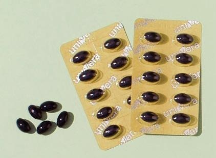 유니베라 글자가 새겨진 노란 PTP 블리스터 두 판과 낱개 검은 연질캡슐이 연두색 바닥에 놓인 컷
