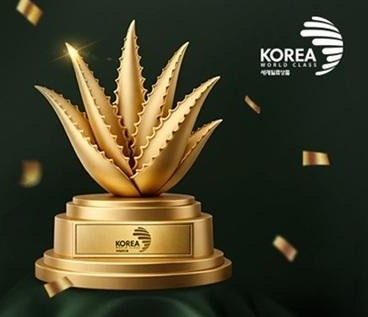 받침에 KOREA 세계일류상품 표시가 새겨진 금색 알로에 트로피와 흩날리는 금박, 오른쪽 위에 KOREA WORLD CLASS 세계일류상품 마크